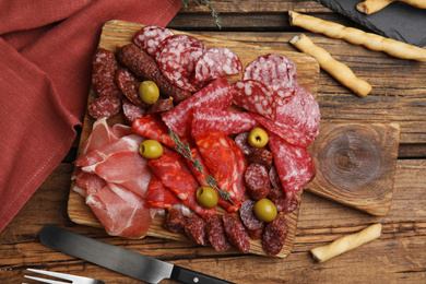 Tasty prosciutto with other delicacies served on wooden table, flat lay