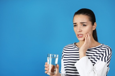 Emotional young woman with sensitive teeth and glass of water on color background. Space for text