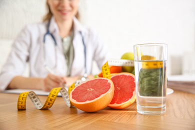 Glass of water, grapefruit, measuring tape and blurred nutritionist on background