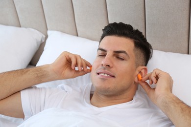 Man inserting foam ear plugs in bed