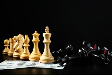 White chess pieces, black fallen ones and money against dark background. Business competition concept