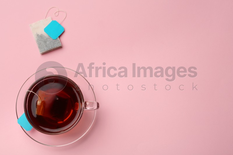 Tea bags and cup of hot drink on pink background, flat lay. Space for text