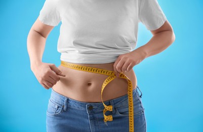 Woman with measuring tape on light blue background, closeup. Overweight problem after New Year party