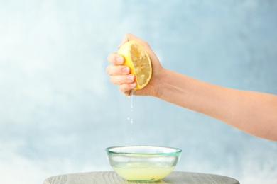 Young woman squeezing lemon juice into bowl on color background