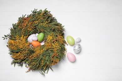 Photo of Festively decorated Easter eggs and nest of beautiful spring flowers on white wooden table, flat lay. Space for text