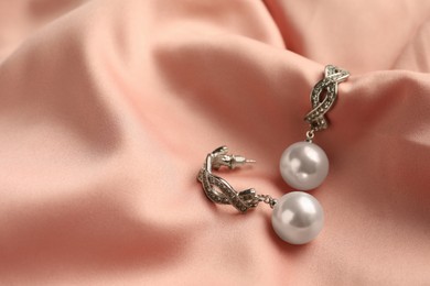 Elegant silver earrings with pearls on pink silk, closeup