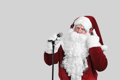 Santa Claus with headphones and microphone on light grey background, space for text. Christmas music