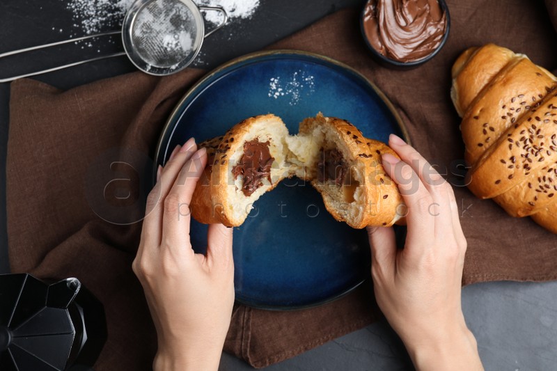Woman eating tasty croissant with chocolate at table, top view