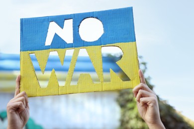 Woman holding poster in colors of Ukrainian flag with words No War outdoors, closeup