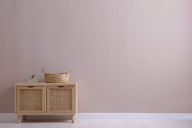 Wooden cabinet with clock and wicker basket near beige wall, space for text. Interior design