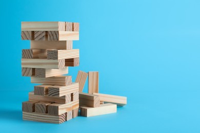 Jenga tower made of wooden blocks on light blue background, space for text