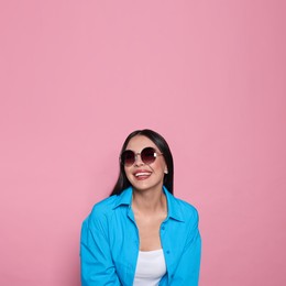 Attractive happy woman in fashionable sunglasses against pink background