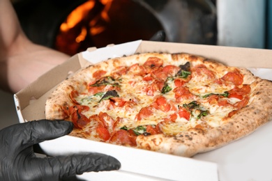 Chef holding delivery box with traditional oven baked Italian pizza in kitchen restaurant, closeup