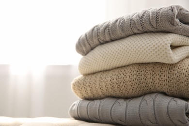 Stack of folded warm sweaters on couch indoors, closeup. Space for text