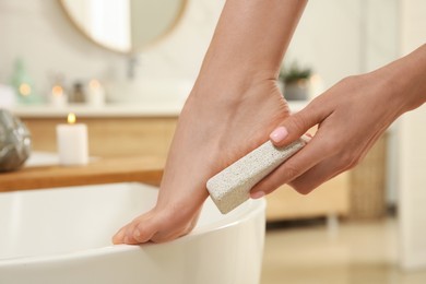 Woman using pumice stone for removing dead skin from feet in bathroom, closeup