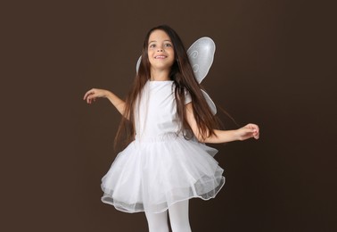 Cute little girl in fairy costume with white wings on brown background