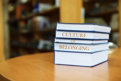Stack of books with phrase Culture of Belonging on table in library. Space for text