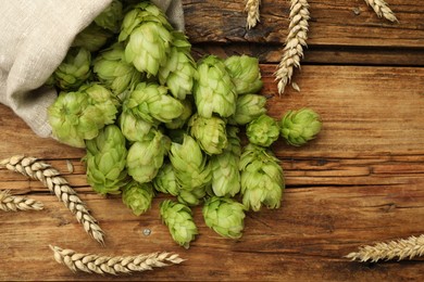 Photo of Sack with fresh green hops and wheat ears on wooden table, flat lay