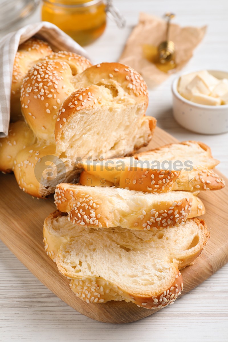 Photo of Cut freshly baked braided bread on white wooden table, closeup. Traditional Shabbat challah