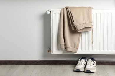 Heating radiator with beige pants and sneakers indoors. Space for text