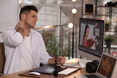 Photo of Tired retoucher at table with modern computer in office
