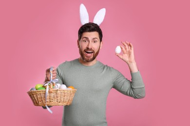 Photo of Portrait of happy man in cute bunny ears headband holding Easter eggs on pink background