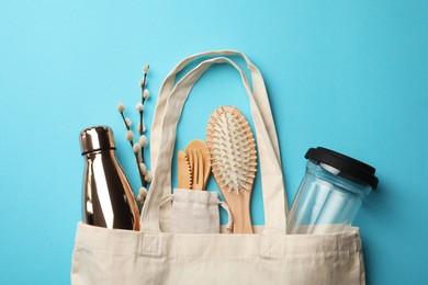 Bag with eco friendly products on light blue background, flat lay. Conscious consumption