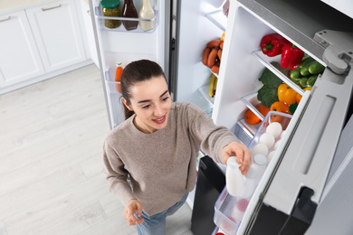 Young woman taking yoghurt out if refrigerator indoors, above view