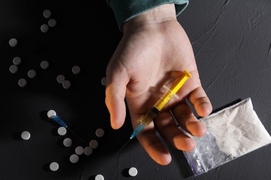 Photo of Addicted man with syringe near drugs at black textured table, top view