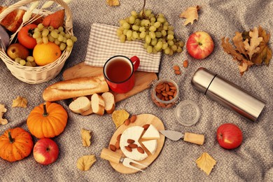 Blanket with picnic basket, snacks and autumn leaves, flat lay
