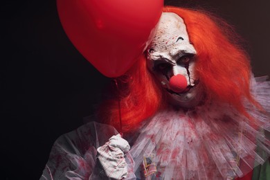 Photo of Terrifying clown with red air balloon on black background. Halloween party costume