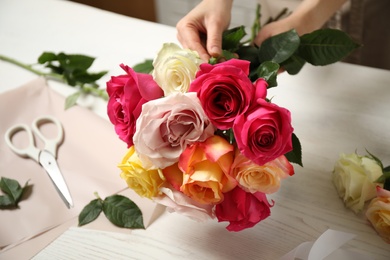 Woman making luxury bouquet of fresh roses at white wooden table, closeup