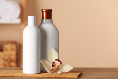 Photo of Bottles of shampoo and flower on wooden table in bathroom, space for text