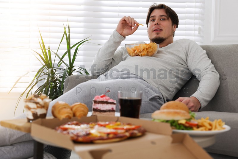 Overweight man with chips on sofa at home