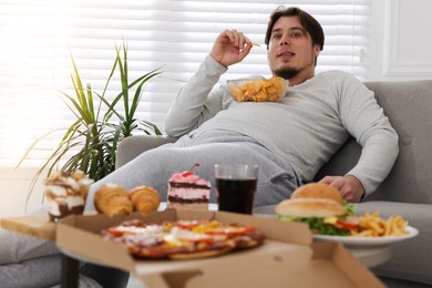 Photo of Overweight man with chips on sofa at home