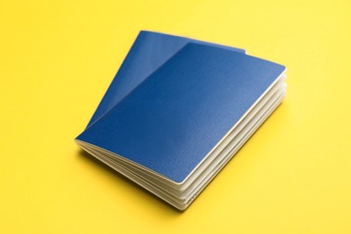 Two blank blue passports on yellow background, closeup