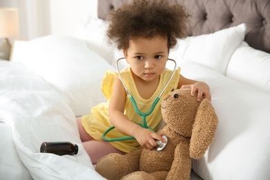 Cute African American child imagining herself as doctor while playing with stethoscope and toy bunny at home