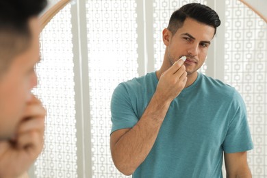 Man applying hygienic lip balm in front of mirror at home