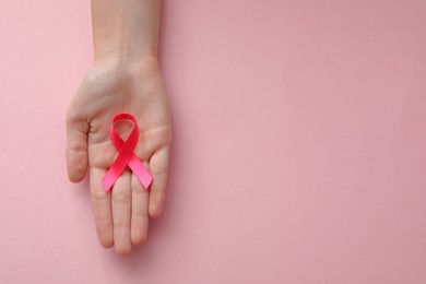 Woman holding pink ribbon on color background, top view with space for text. Breast cancer awareness concept