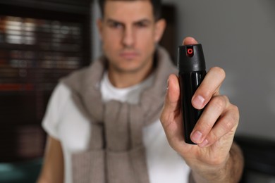 Man using pepper spray indoors, focus on hand