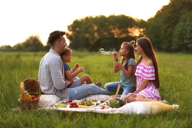 Happy family having picnic in park at sunset