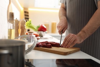 Photo of Man cutting meat to make bouillon in kitchen, closeup. Homemade recipe