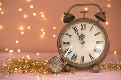 Vintage clock with decor on pink table against blurred Christmas lights, closeup. New Year countdown