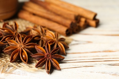 Many aromatic anise stars and cinnamon sticks on white wooden table, closeup