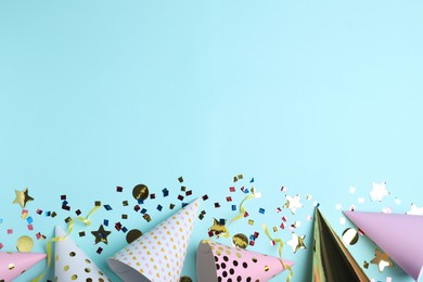 Flat lay composition with party hats and confetti on light blue background, space for text. Birthday decor