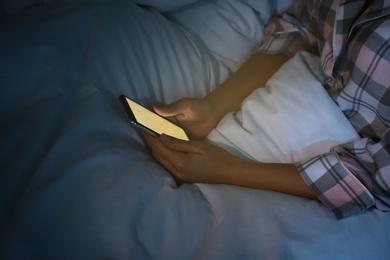 Woman using smartphone in bed at night, closeup. Nomophobia and sleeping disorder problem