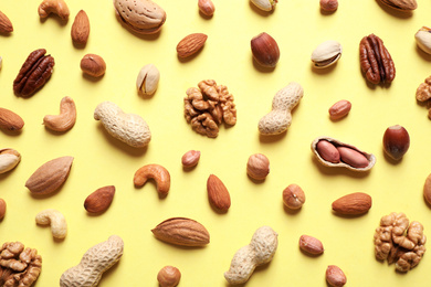 Photo of Different delicious nuts on yellow background, flat lay