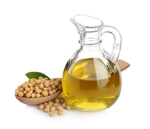 Glass jug of oil, wooden spoon and soybeans on white background