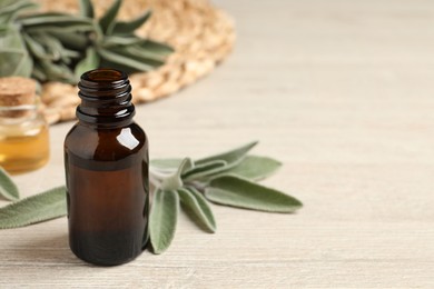 Bottle of essential sage oil and leaves on wooden table. Space for text