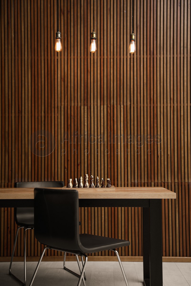 Photo of Modern table with chess near wooden wall